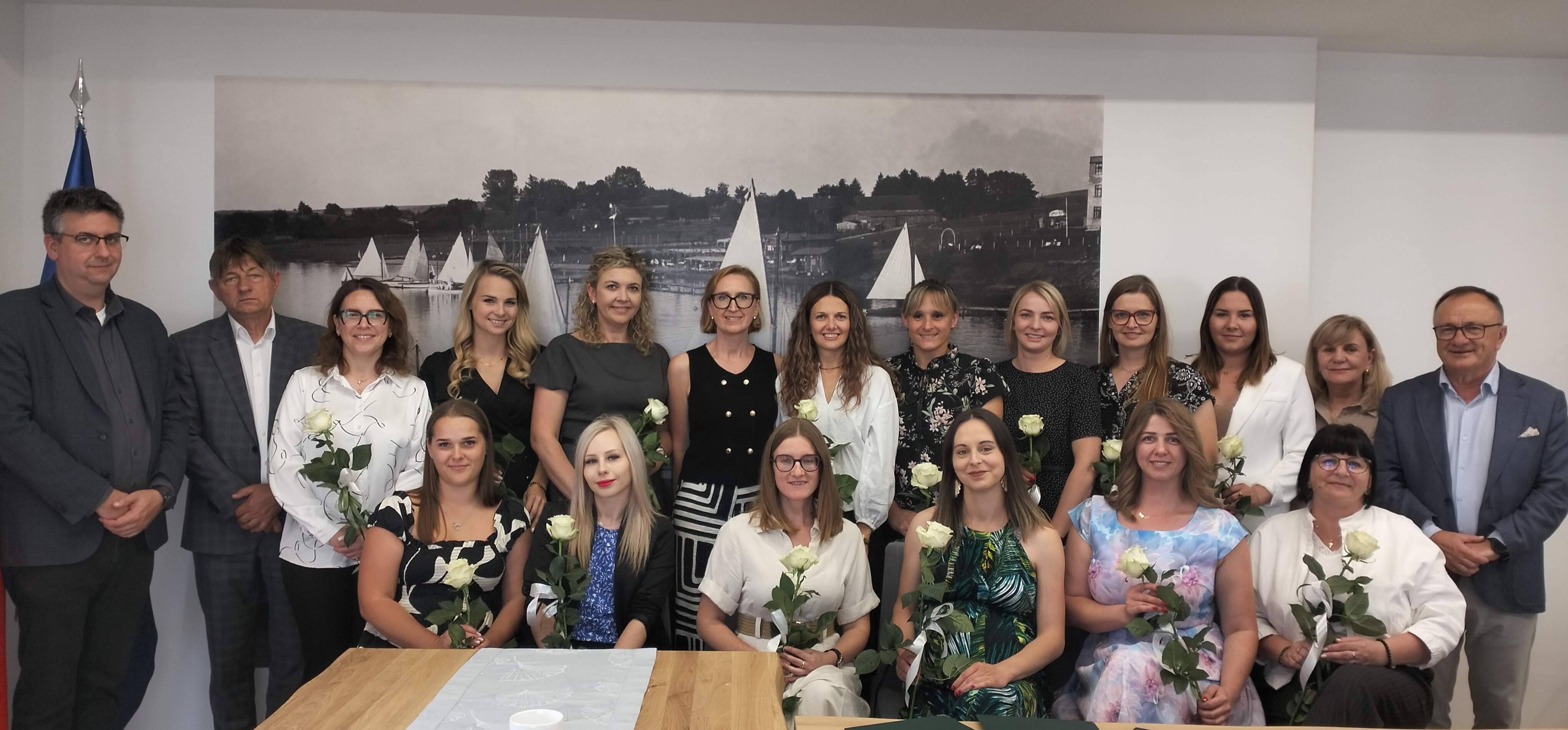 Nauczycielki trzymające kwiaty stoją w&nbsp;dw&oacute;ch rzędach na&nbsp;tle ściany w&nbsp;towarzystwie W&oacute;jta, Zastępcy W&oacute;jta, Przewodniczącego Rady Gminy i&nbsp;Dyrektora GZO.