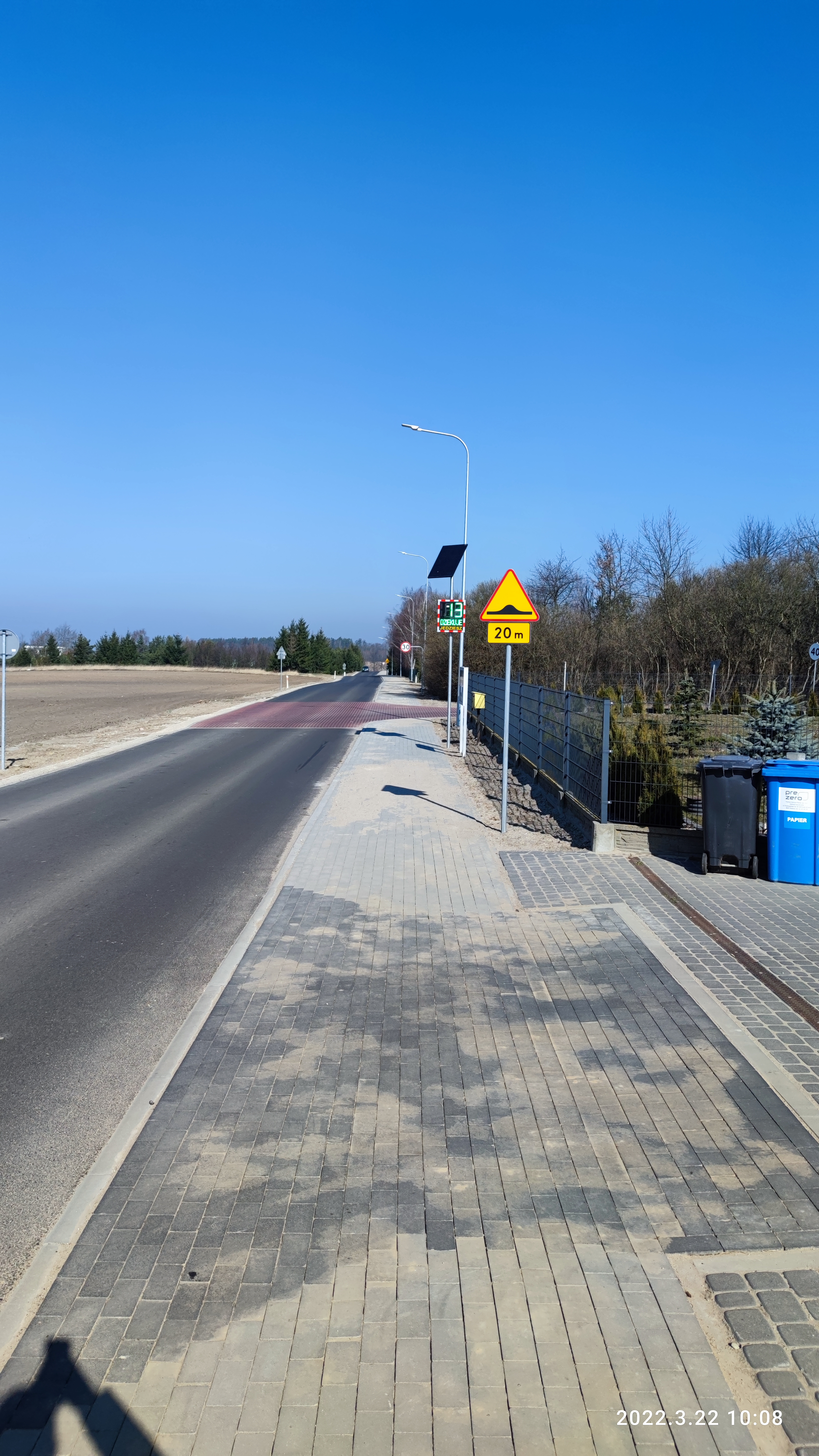 ulica Podmiejska z nową nawierzchnią bitumiczną oraz chodnikiem. W tle radar z aktywną tablicą informującą o prędkości pojazdu